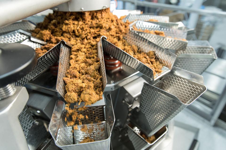 A machine making light brown Pulled Oats meat alternative