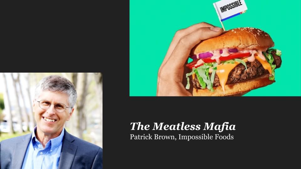 A white man with gray hair and glasses smiling into camera. Brown hand holding a cheeseburger